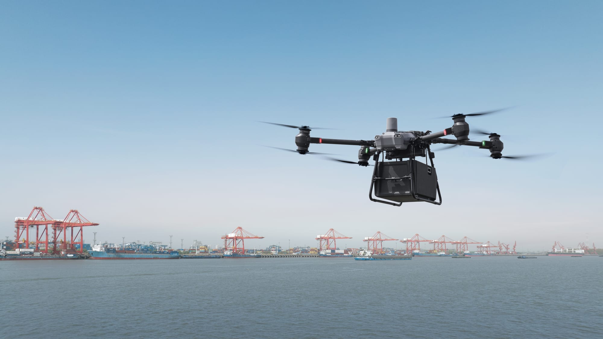 Image of a delivery drone over open water near a cargo ship depot.