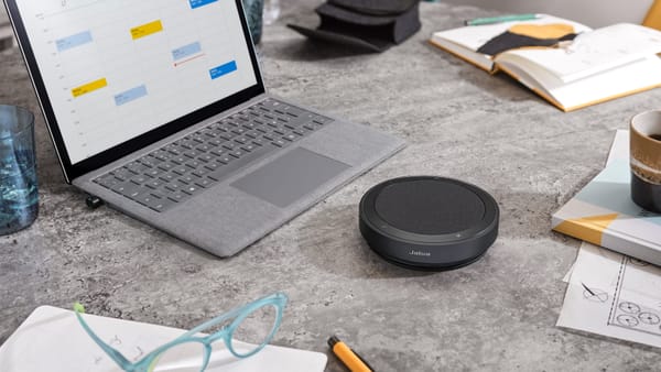 Jabra Speak2 75 Bluetooth speakerphone sitting on a table next to a laptop