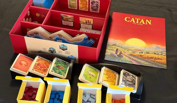 The open 6th Edition Catan box, with its cards, rules, and pieces organised on a black tablecloth.