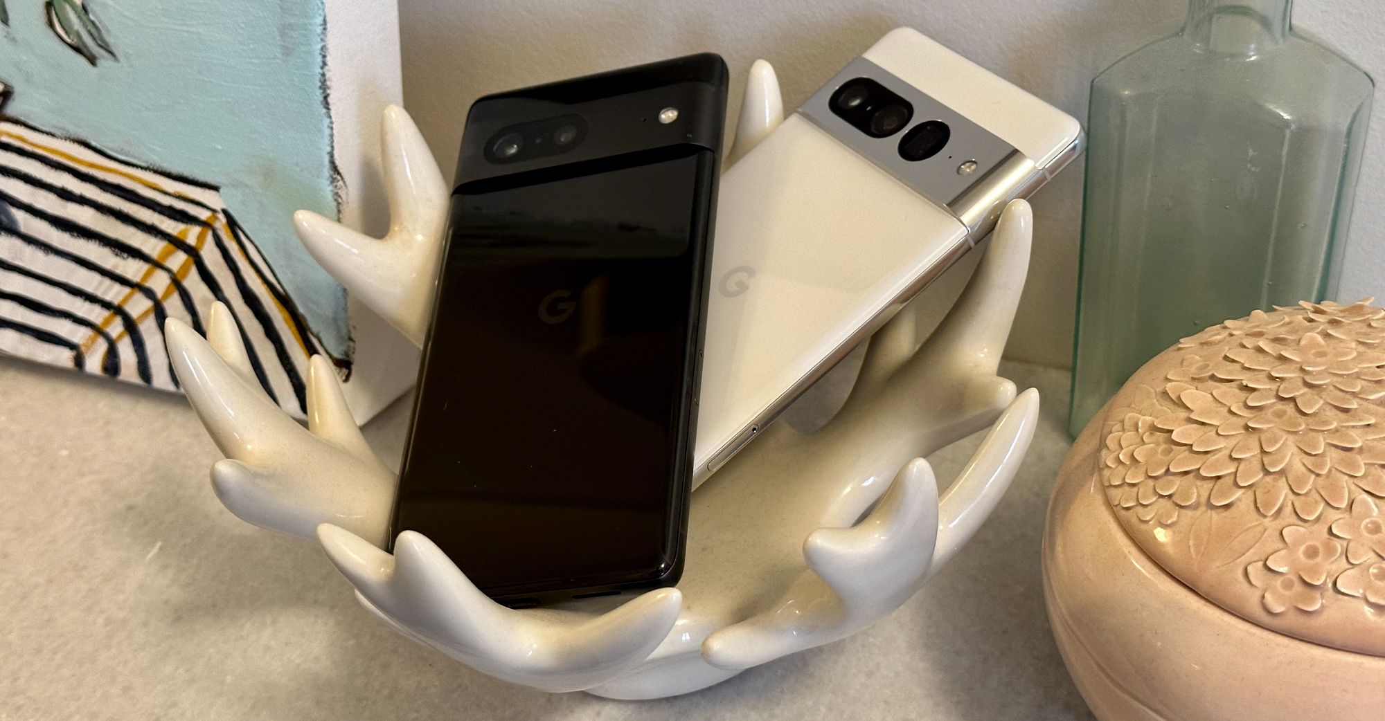 Two phones resting in a fancy dish on a sidetable. The phones are a black Pixel 7 and a while Pixel 7 Pro.