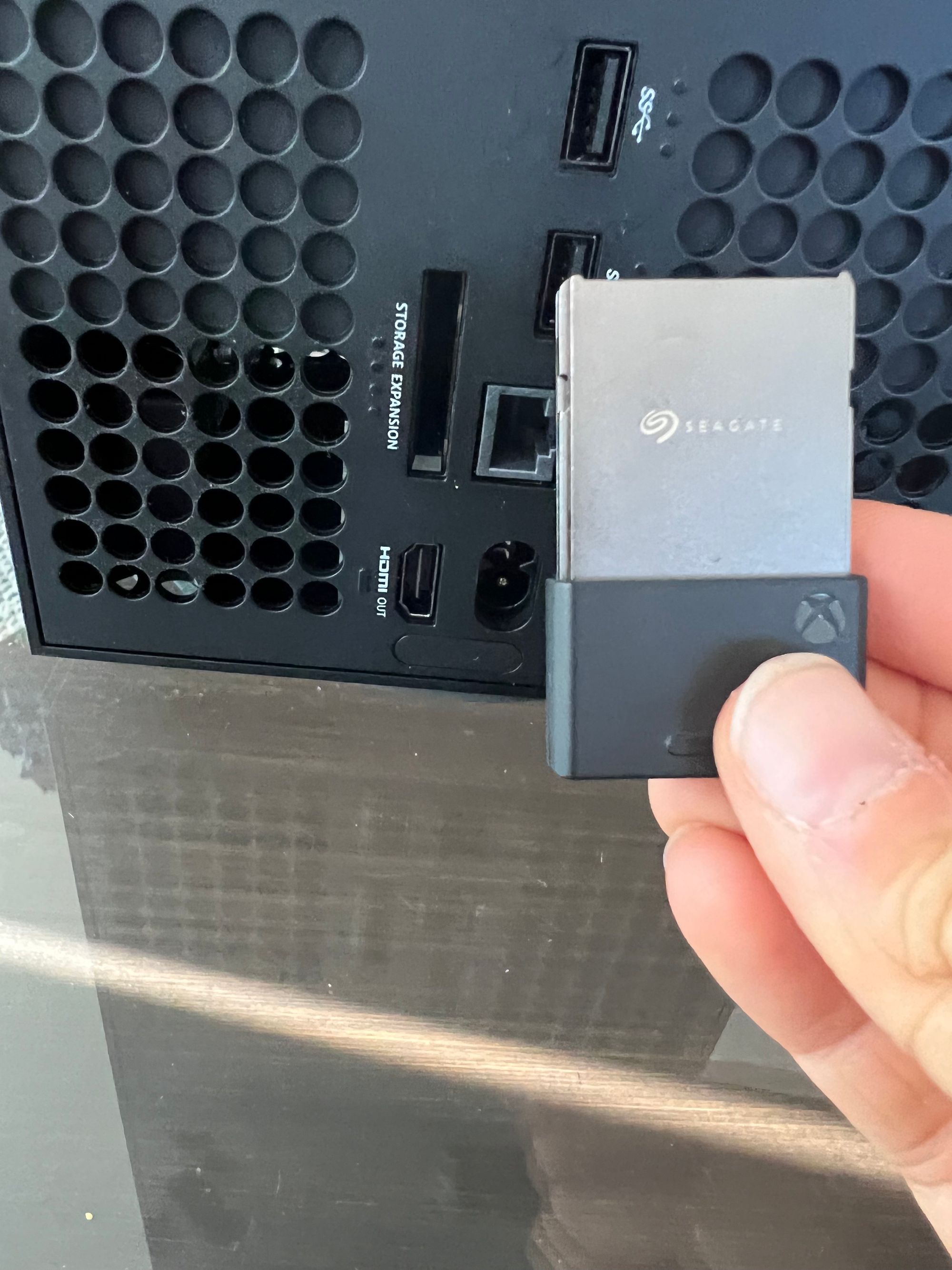 A hand holding a 2TB Seagate Expansion Card next to the expansion card slot on an Xbox Series X.